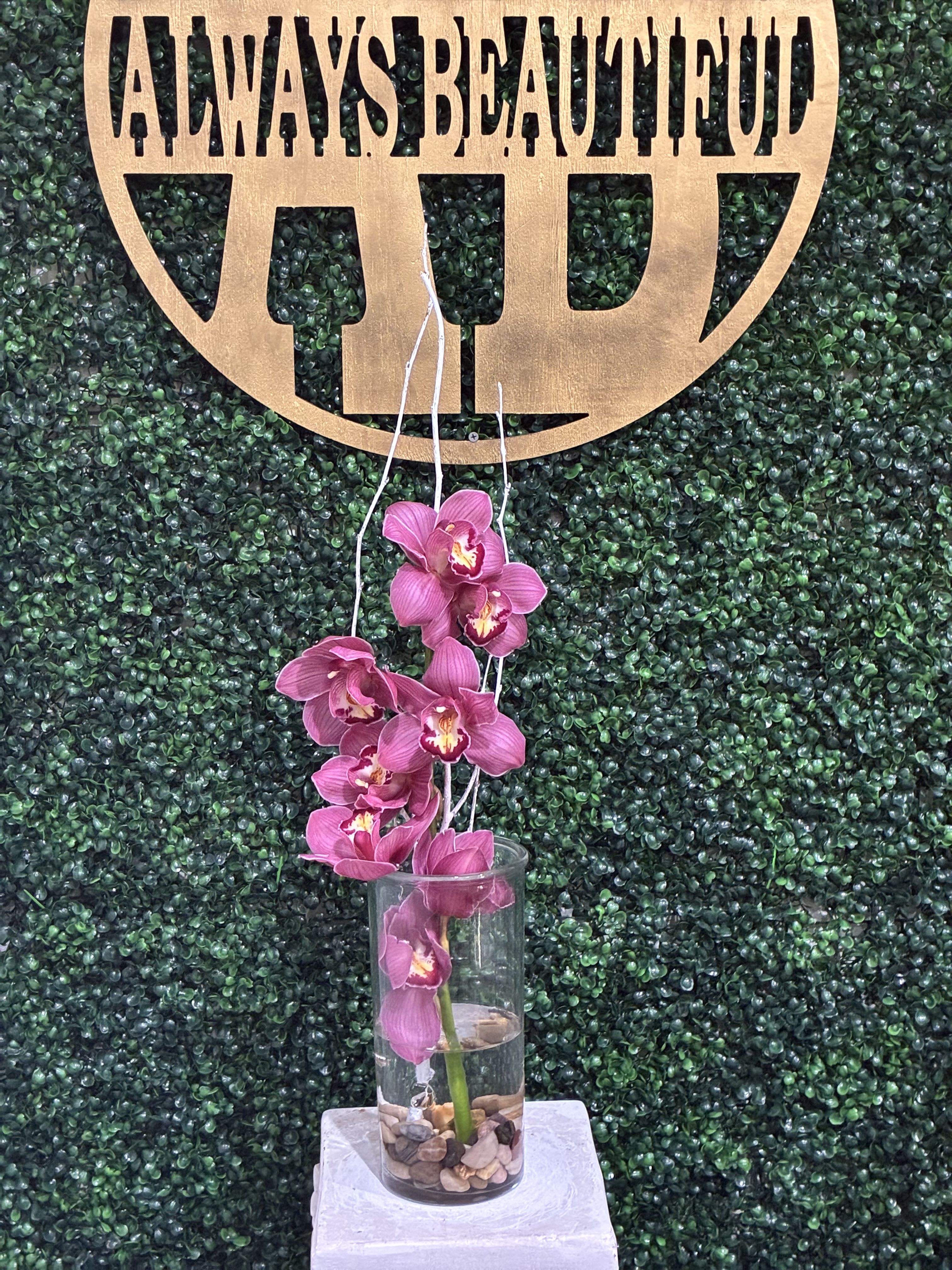 Pink orchids in a clear glass vase against a green backdrop