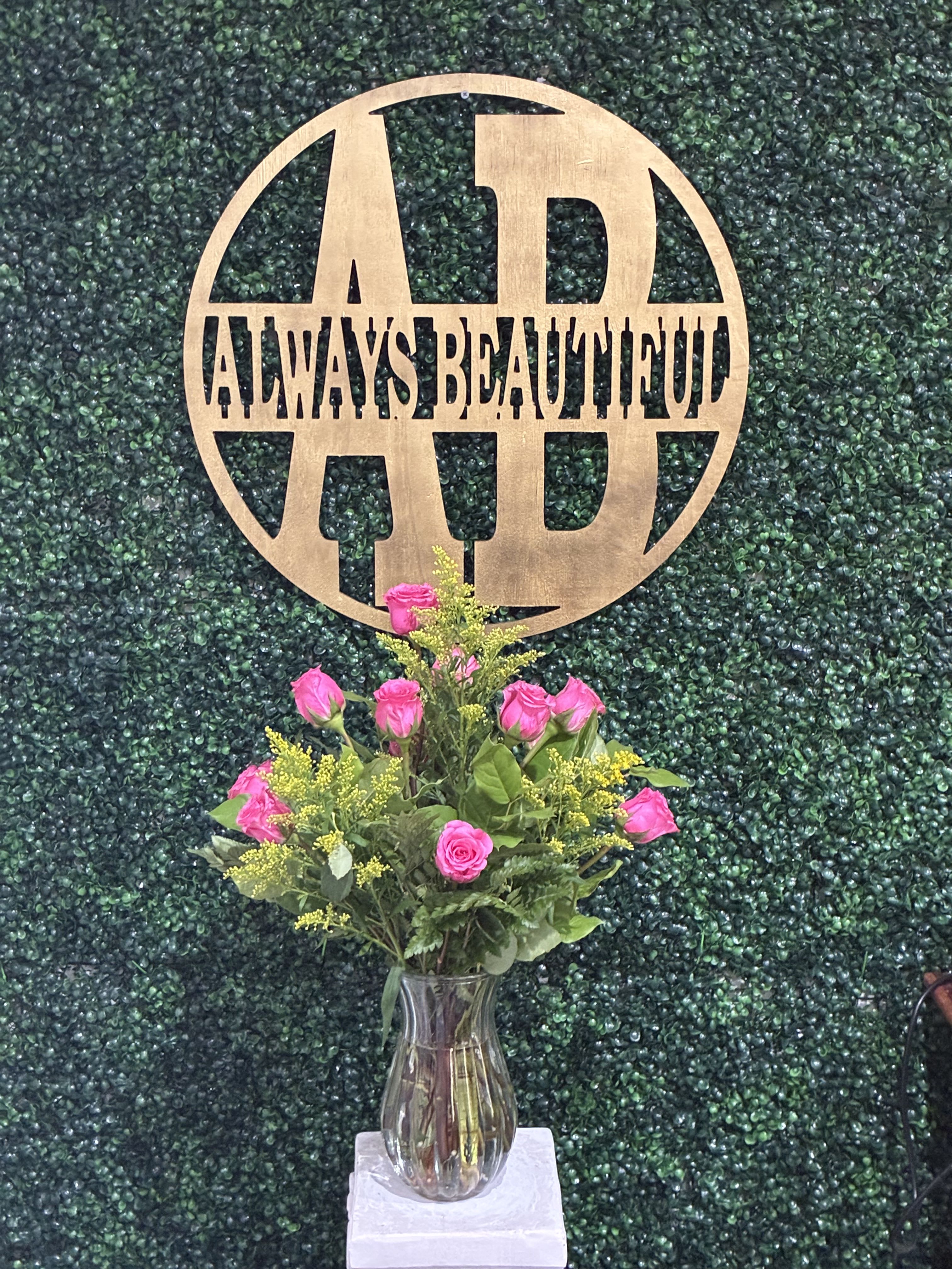 Pink rose bouquet in a clear vase with a wooden monogram sign behind it