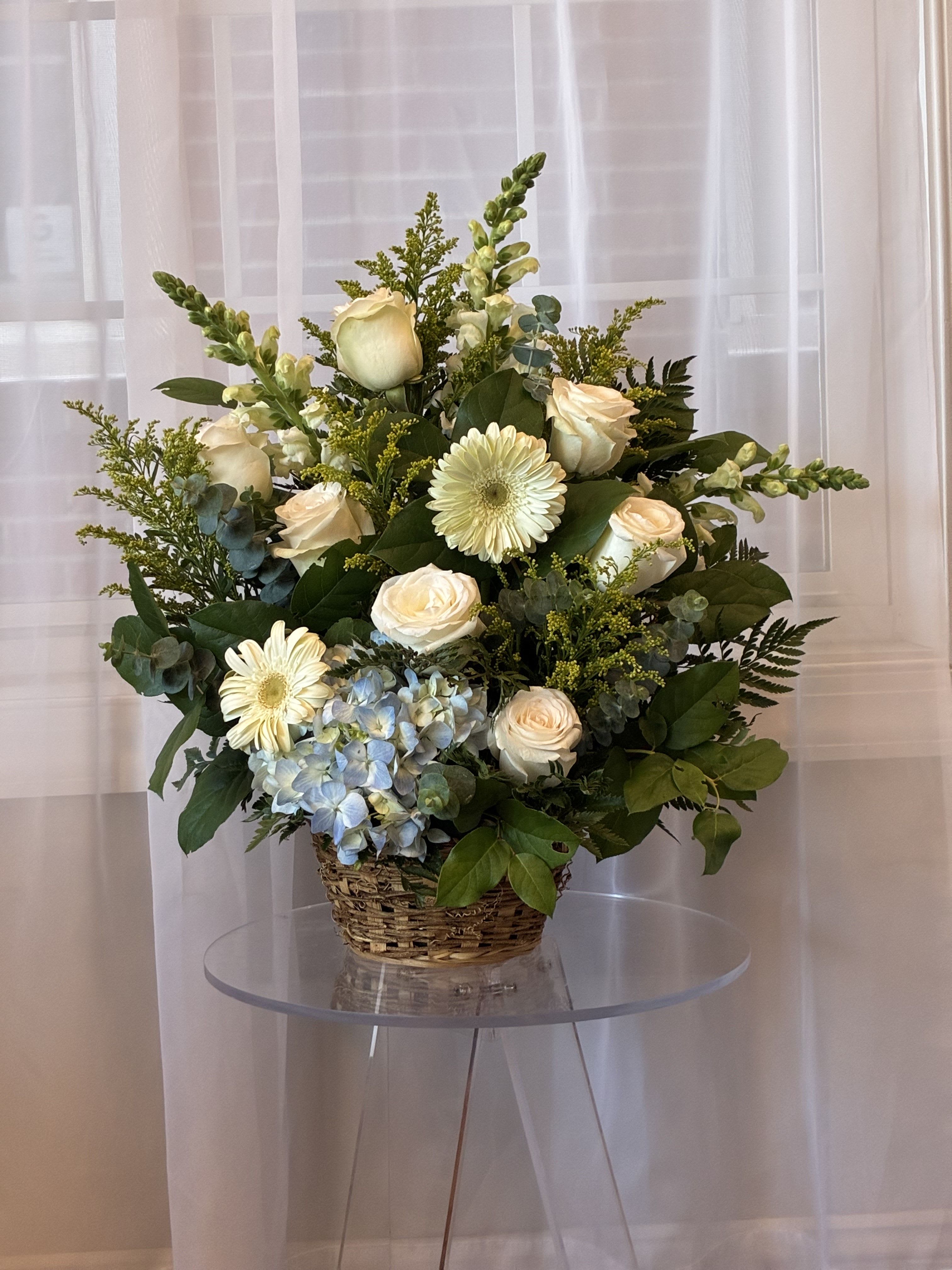 Basket arrangement of cream roses, white gerberas, and blue hydrangea