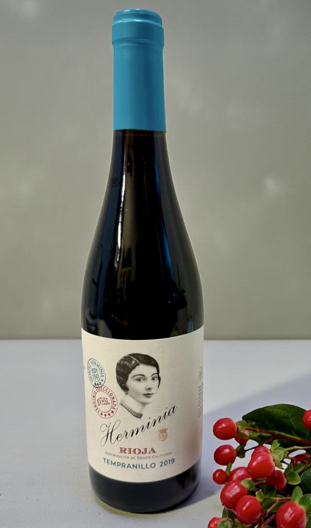 Bottle of red wine with a blue cap and berry sprig beside it