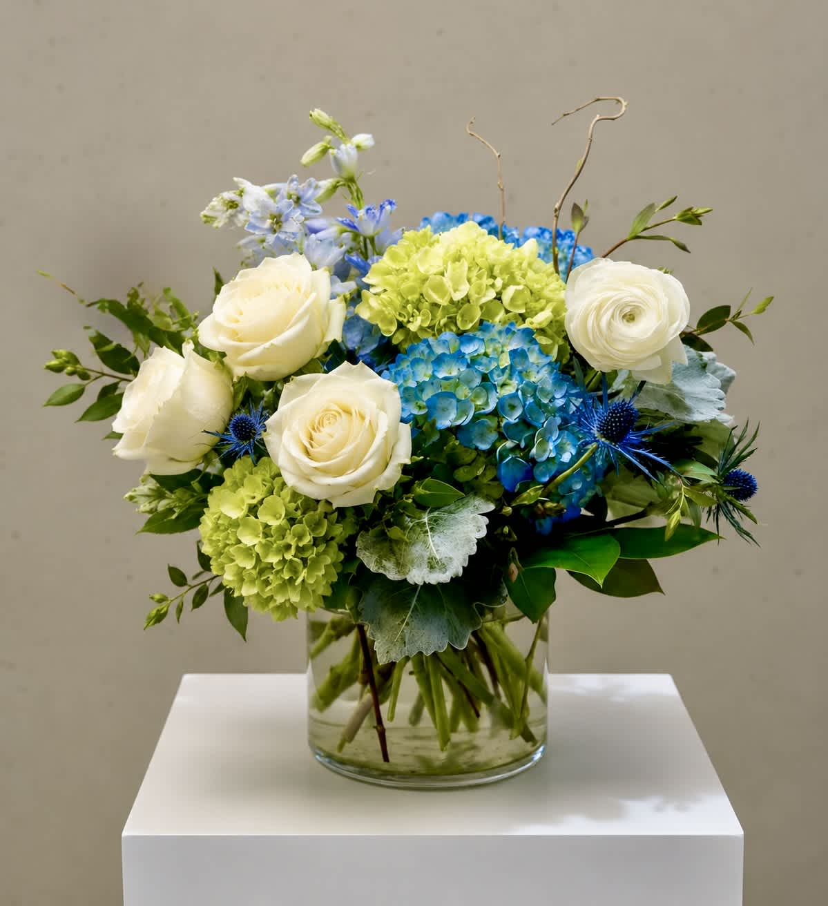 Blue and green floral arrangement with white roses in a glass vase