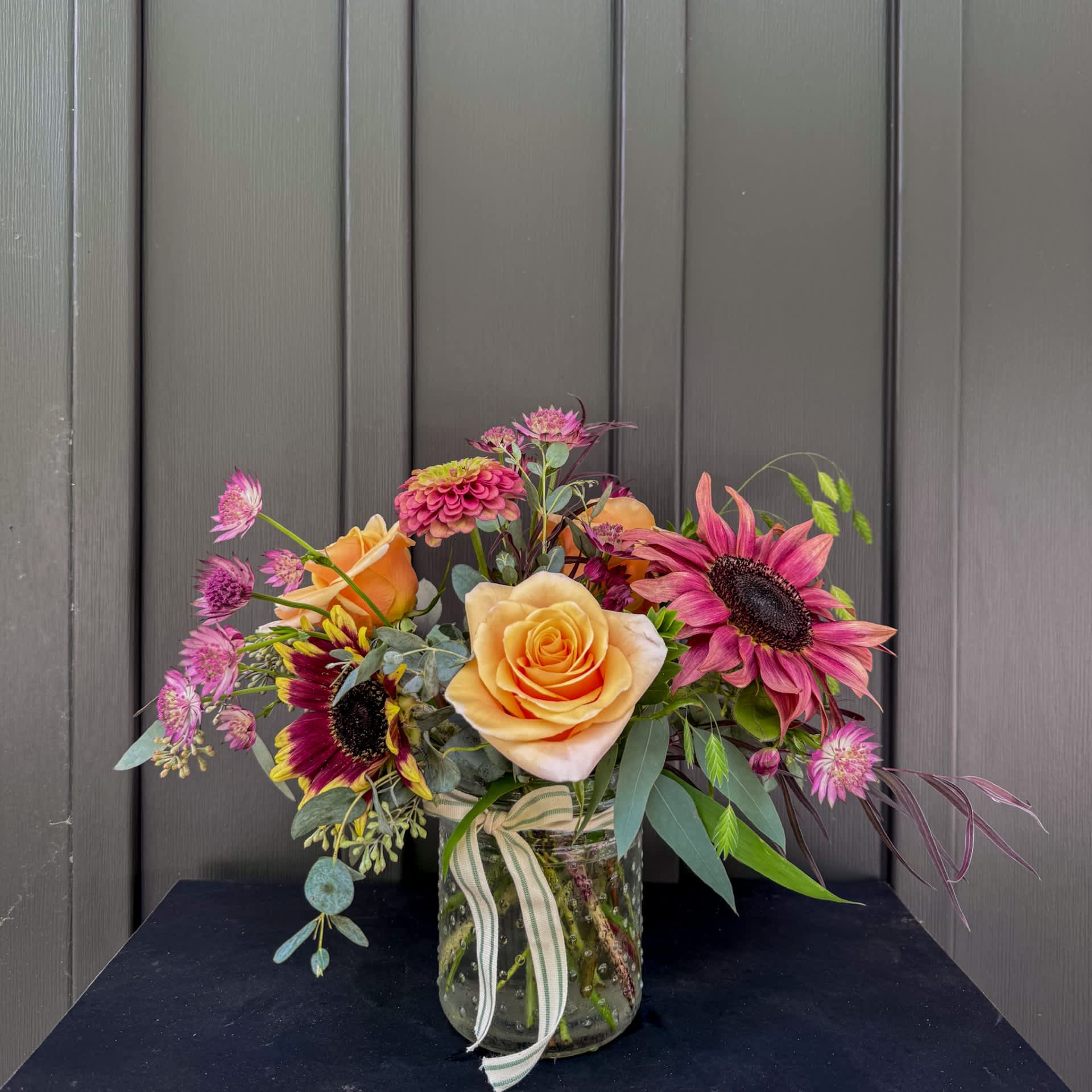 Mixed bouquet of roses and sunflowers in a glass jar vase