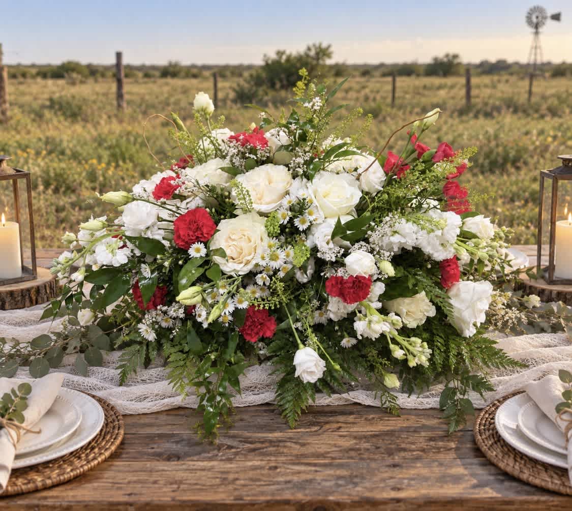 Large white and red floral centerpiece on a rustic table outdoors