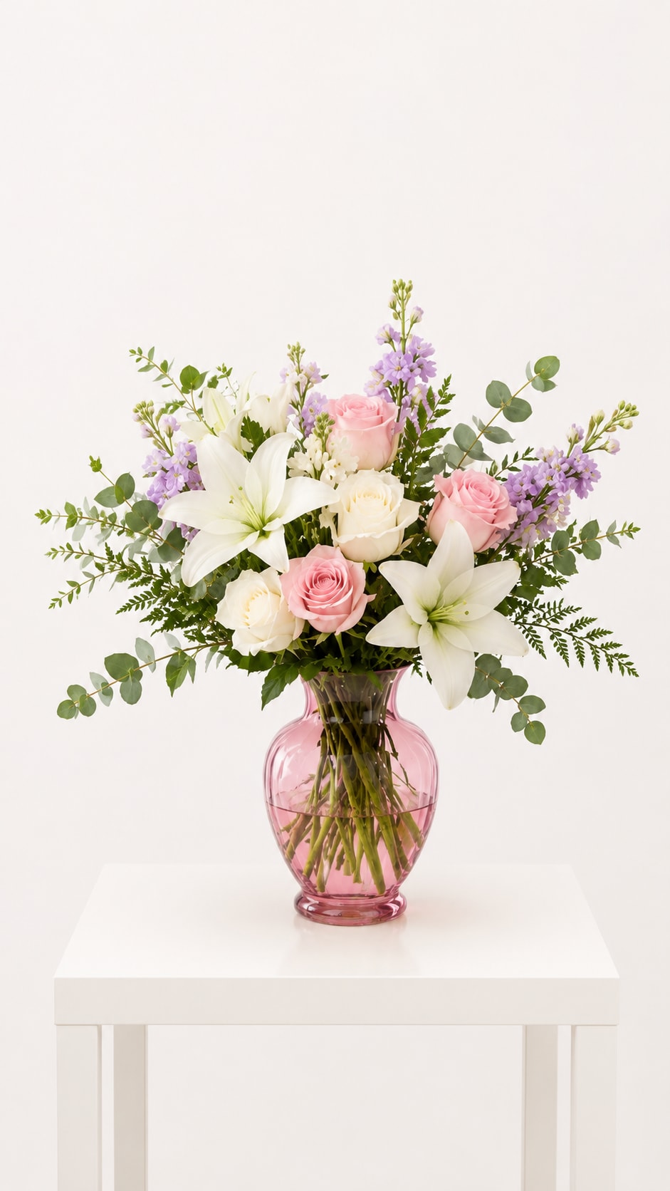 Blush Lily Garden Vase - Soft, elegant, and timeless, this fresh floral arrangement features white lilies, blush pink roses, white roses, lavender stock, eucalyptus, and seasonal greenery designed in a pink glass vase. Its natural garden-style design creates a romantic and sophisticated look perfect for celebrating life’s sweetest moments.  Perfect for gifting, home décor, birthdays, anniversaries, and especially Mother’s Day flowers delivery in Naples, Bonita Springs, Fort Myers Beach, and Southwest Florida.  Available for local flower delivery throughout Naples, Bonita Springs, Estero, Fort Myers and Fort Myers Beach.  Designer’s Choice: Each arrangement is uniquely designed using the freshest seasonal flowers available. Flower varieties, colors and containers may vary while maintaining the overall style, value and beauty of the design.