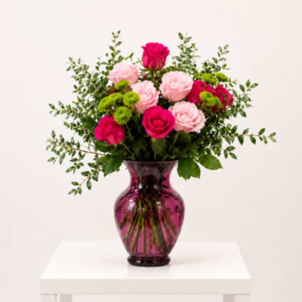 Fuchsia Garden Glow - A fresh and naturally styled floral arrangement designed in a modern translucent fuchsia vase, featuring hot pink roses, light pink roses, green button mini pom chrysanthemums, and lush premium greenery. Designed with a soft garden-inspired feel, visible stems, and clear water for an elegant and organic presentation.  Perfect For: Mother’s Day, Birthday, Thinking of You, Thank You, Get Well, Just Because, Elegant Home Décor  Available for local flower delivery throughout Naples, Bonita Springs, Estero, Fort Myers and Fort Myers Beach.  Designer’s Choice: Each arrangement is uniquely designed using the freshest seasonal flowers available. Flower varieties, colors and containers may vary while maintaining the overall style, value and beauty of the design.