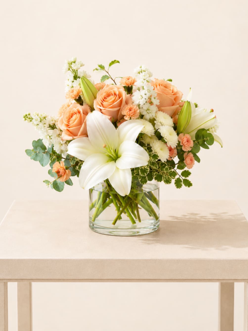 Peach roses and white lilies arranged in a clear glass vase