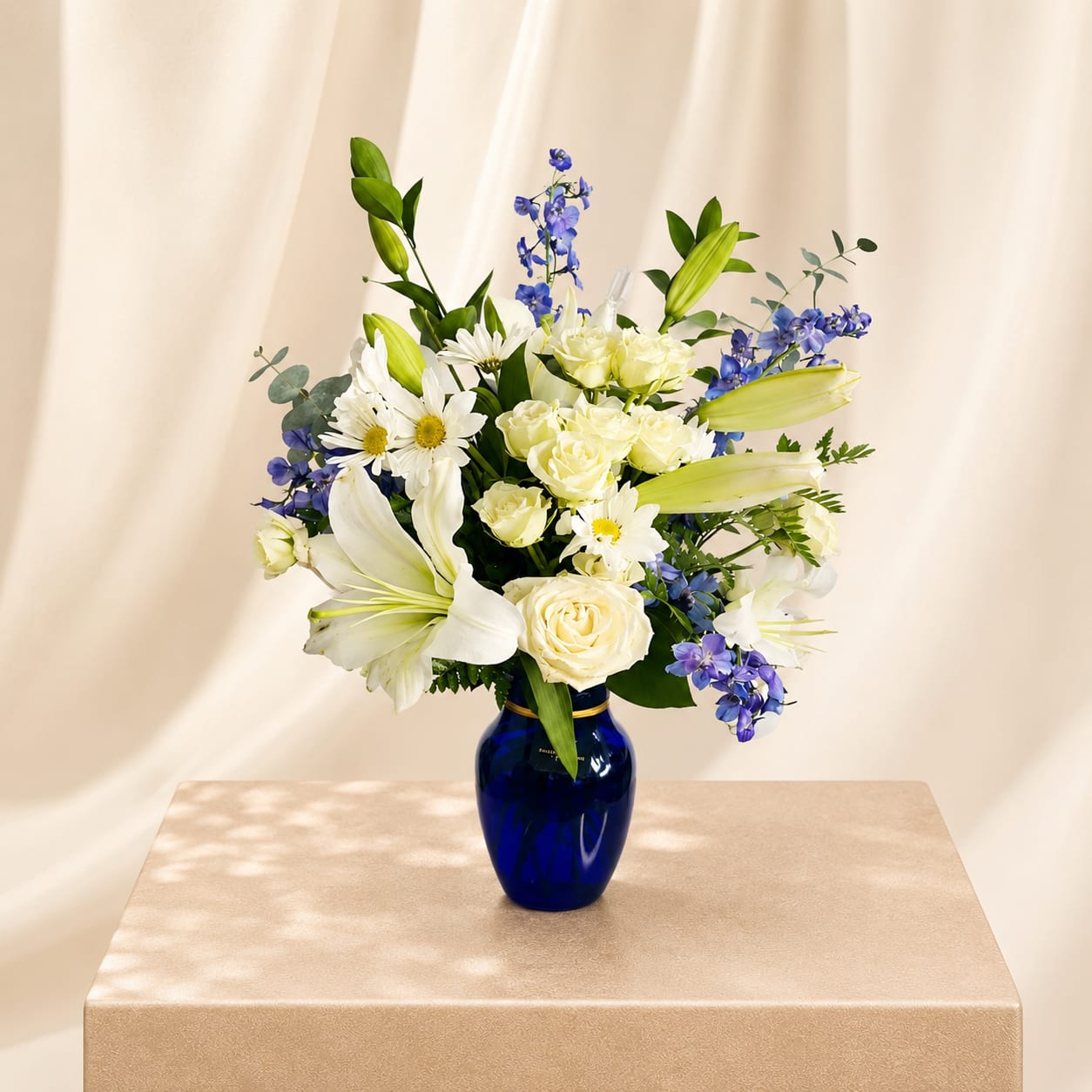 Twillight Grace - Elegant white lilies and rich lavender-toned blooms come together in a striking cobalt blue vase, creating a design that feels both peaceful and refined. This arrangement is a beautiful expression of calm and comfort, with a touch of timeless beauty.  Perfect  for: Sympathy, Get Well Soon, Mother’s Day, Thank You, New Baby, Thinking of You, Birthday.  Available for local flower delivery throughout Naples, Bonita Springs, Estero, Fort Myers and Fort Myers Beach.  Designer’s Choice: Each arrangement is uniquely designed using the freshest seasonal flowers available. Flower varieties, colors and containers may vary while maintaining the overall style, value and beauty of the design. 