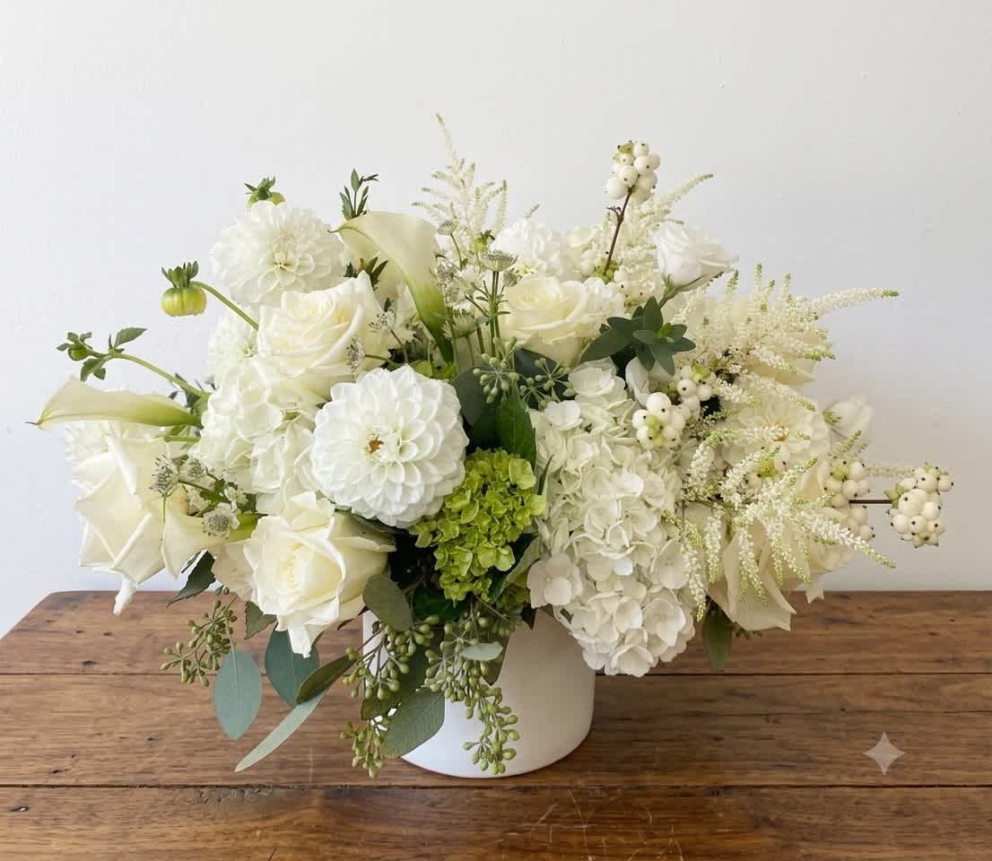 White floral arrangement in a white vase with roses, hydrangeas, and calla lilies