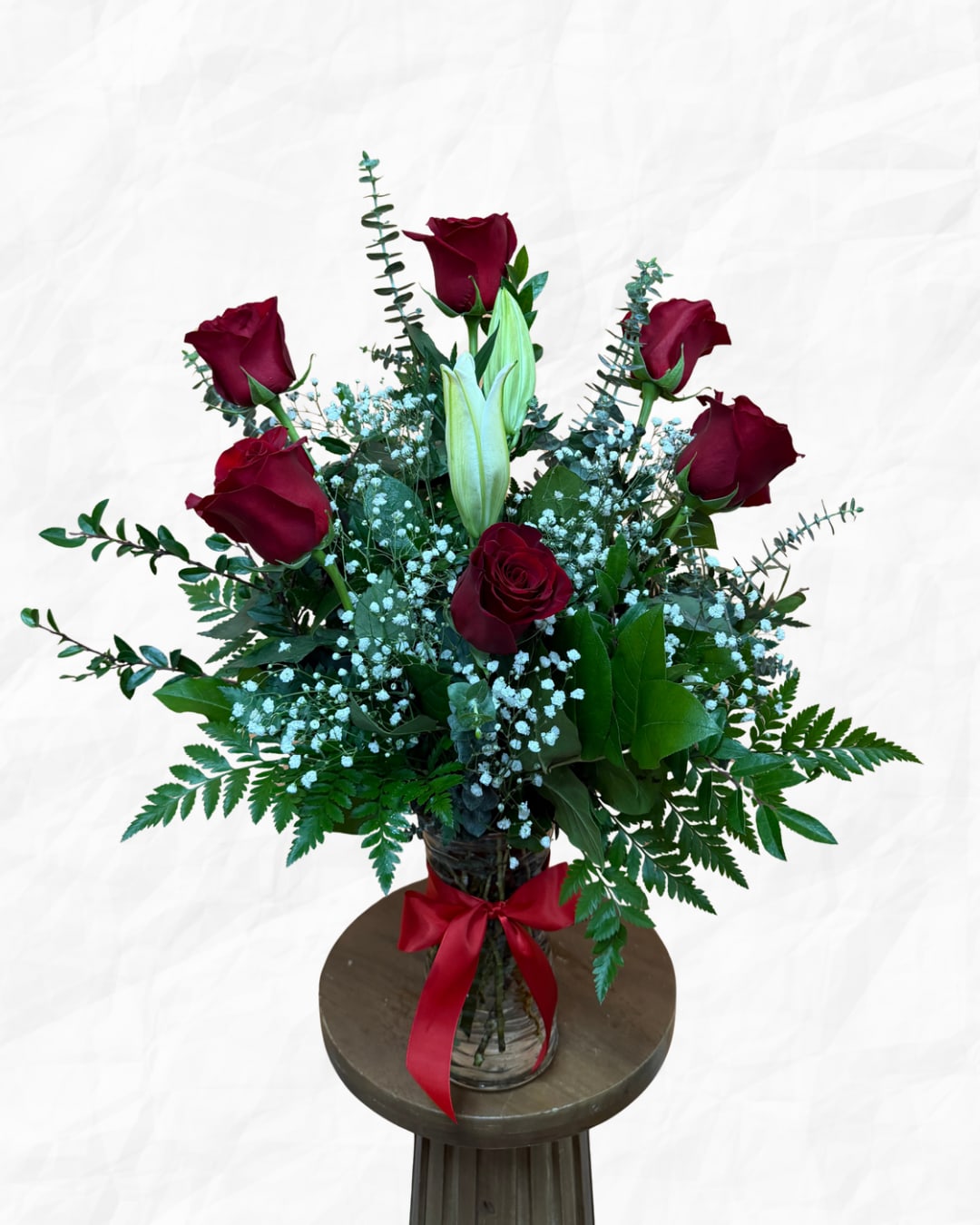 Bouquet of red roses and white lilies in a glass vase with a red ribbon