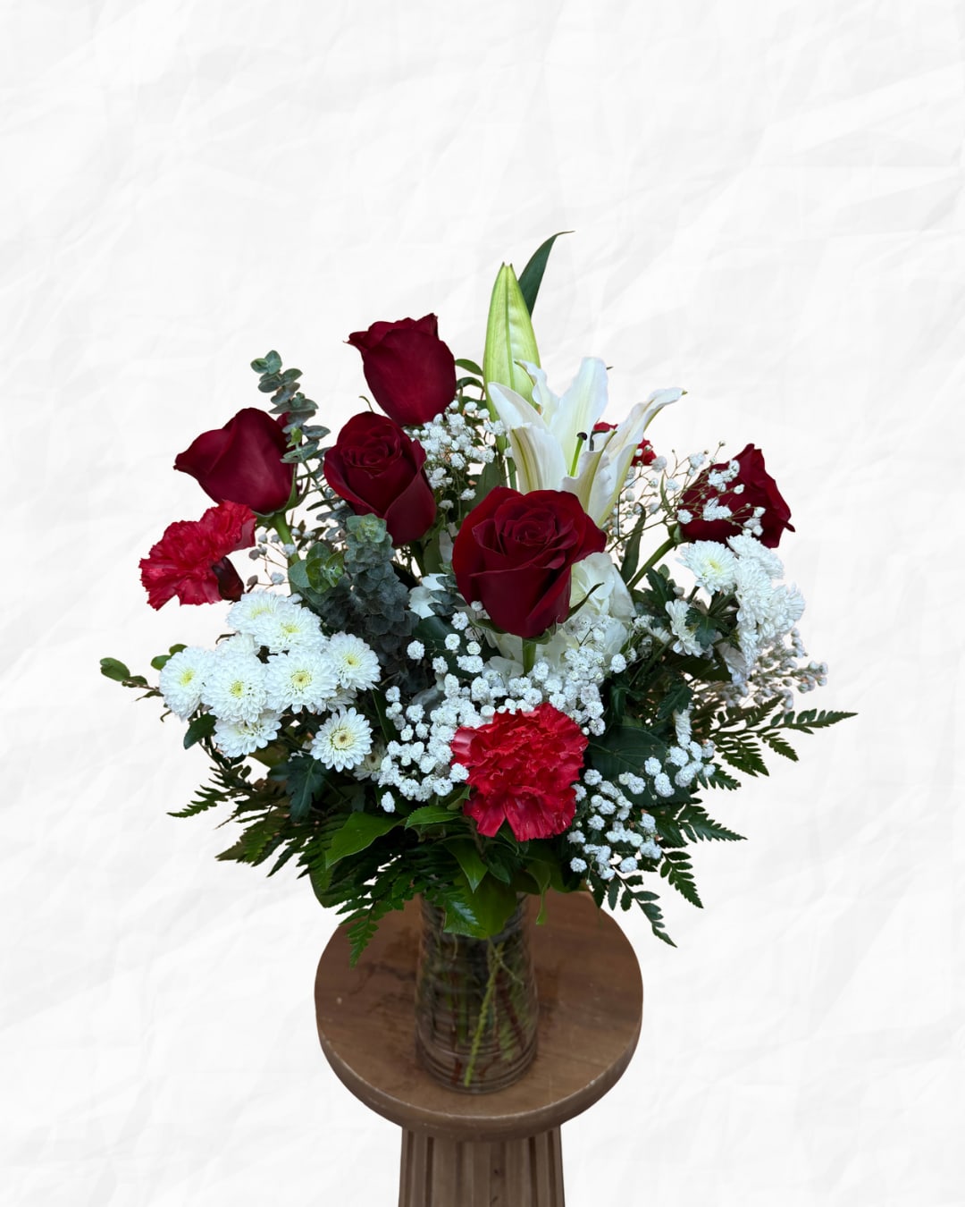 Bouquet of red roses, white lilies, and white daisies in a glass vase