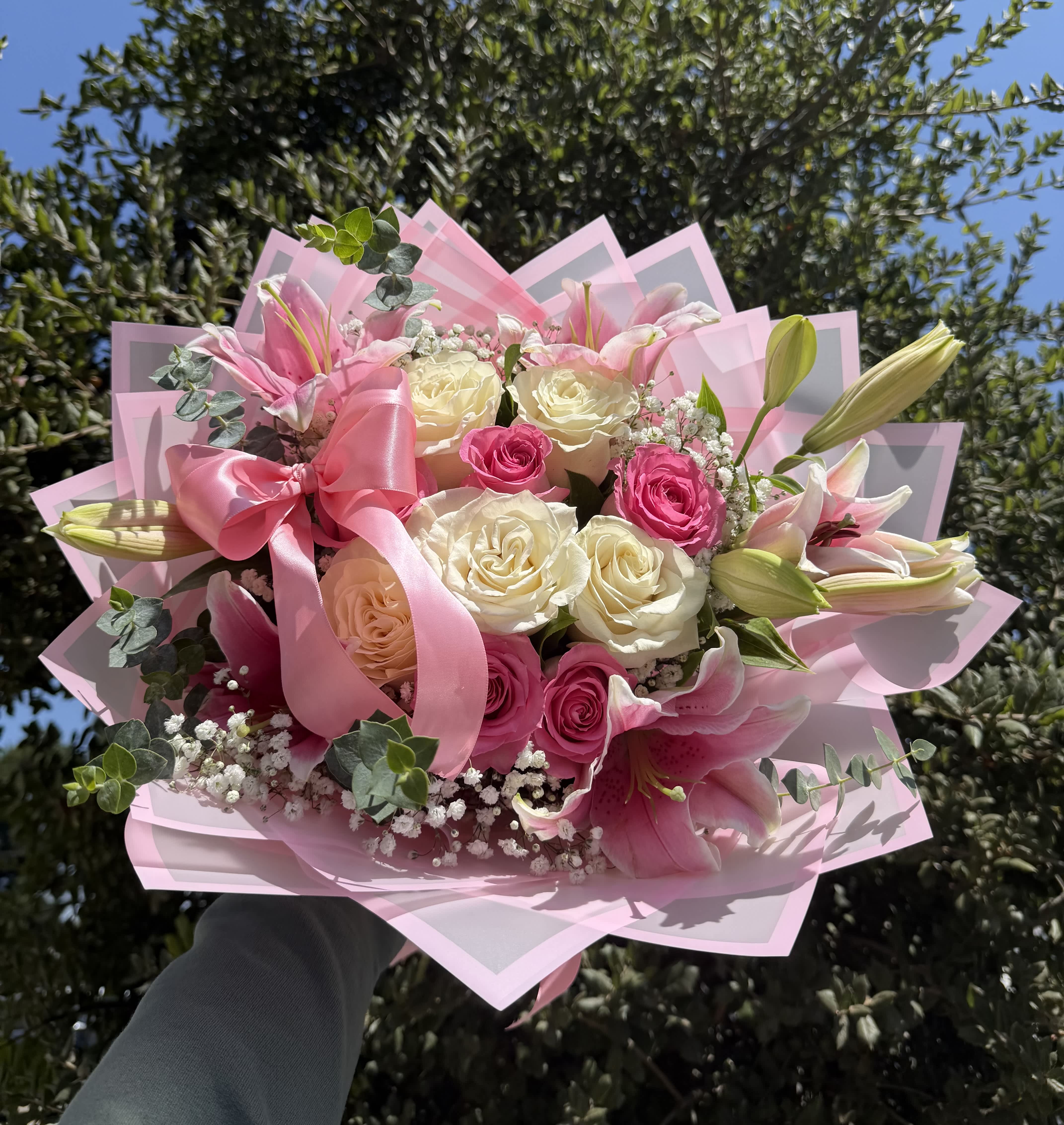 Pink and white bouquet of roses and lilies wrapped with a pink ribbon