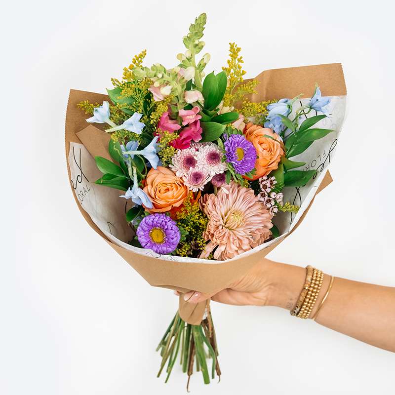 Handheld bouquet of mixed pastel flowers wrapped in brown paper