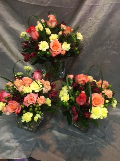 Three mixed flower arrangements with pink and peach roses in clear vases