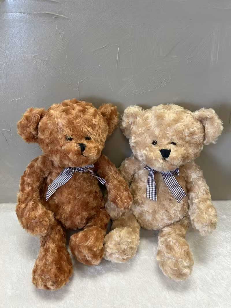 Teddy Bear Medium Size - cuddly plush teddy bear make a heartwarming gift for a new baby, birthday, or to say "thinking of you." This medium-sized teddy bear arrangement is presented as a pair-one warm brown and one cream-each with soft curly fur and a sweet gingham ribbon bow at the neck, creating an instantly comforting, affectionate look that reads as both playful and sincere.  The bears sit side by side in a simple, clean presentation that highlights their plush texture and friendly faces; the neutral brown and white palette works well for baby showers, get-well wishes, or anytime you want to send a tender, reassuring gift. The gingham bows add a classic, homey touch that complements most nursery or bedside décor.  Perfect for the person who appreciates a gentle, personal surprise, these plush companions are the kind of gift that will make someone feel seen and comforted. Medium size makes them easy to display or cuddle; order now to send a soft, lasting hug when flowers aren't quite the right fit.