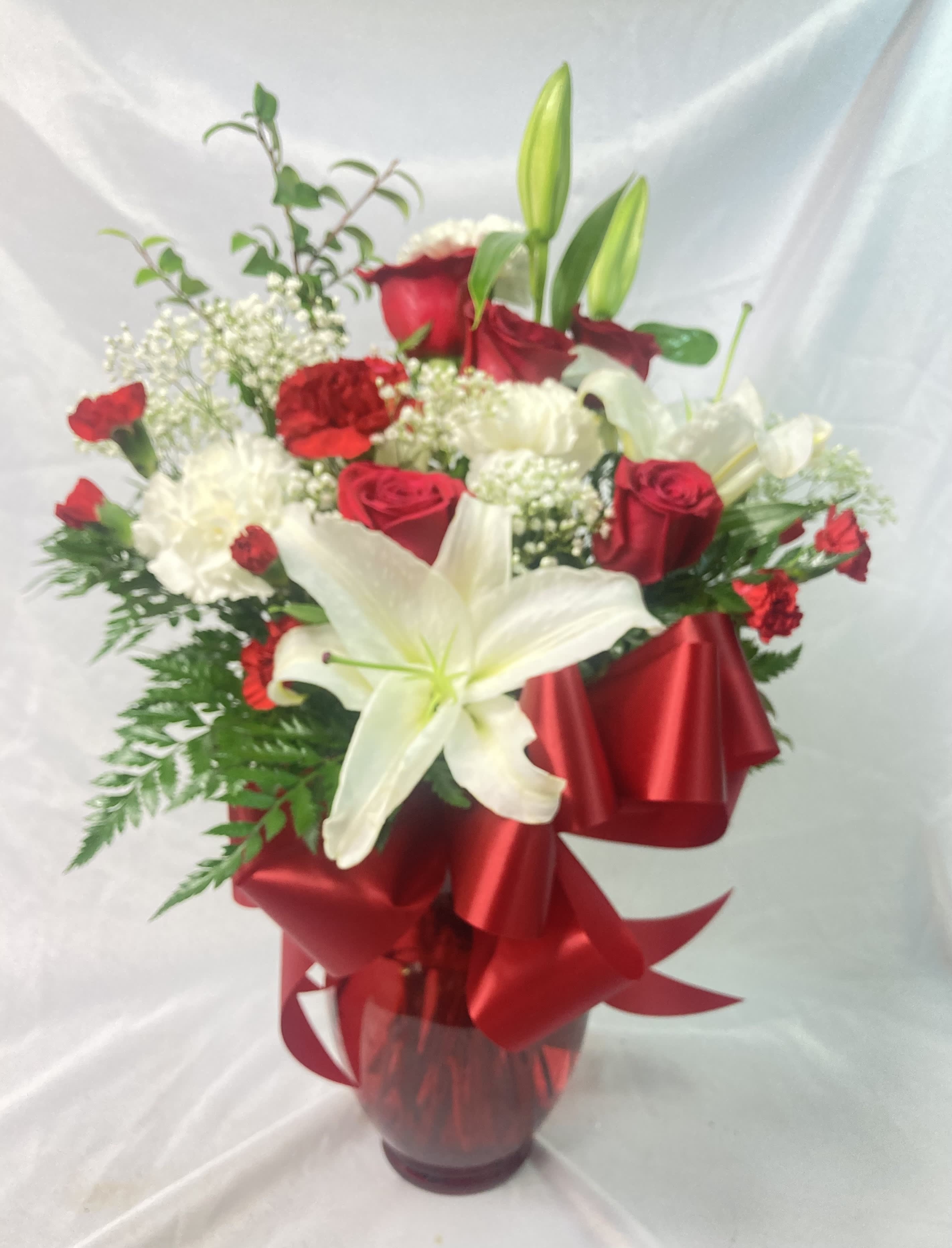 Red and white flower arrangement in a glass vase with a red ribbon