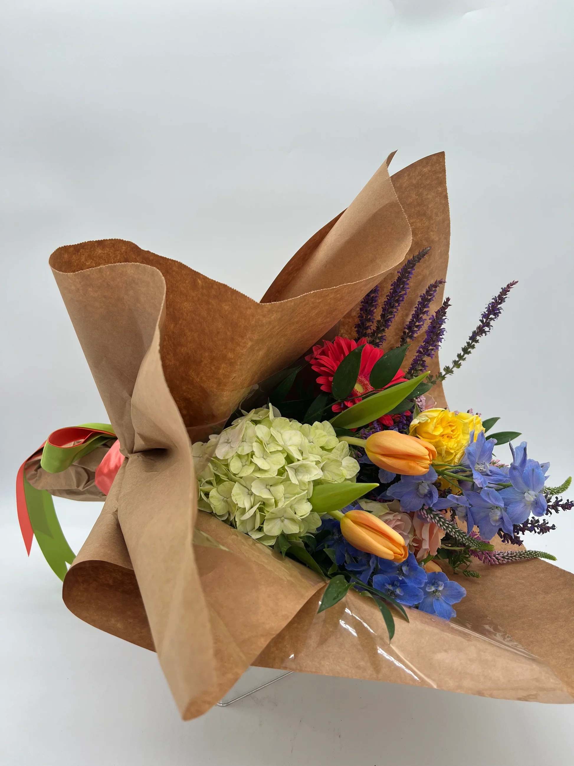 Wrapped bouquet of mixed hydrangea, tulips, roses, and blue flowers in kraft paper