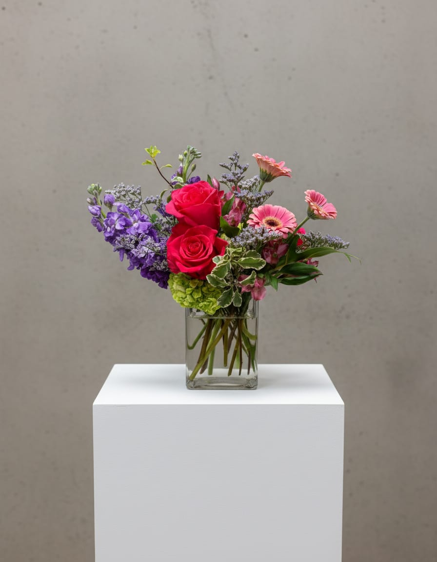 Mixed bouquet of pink roses, purple flowers, and gerbera daisies in a glass vase