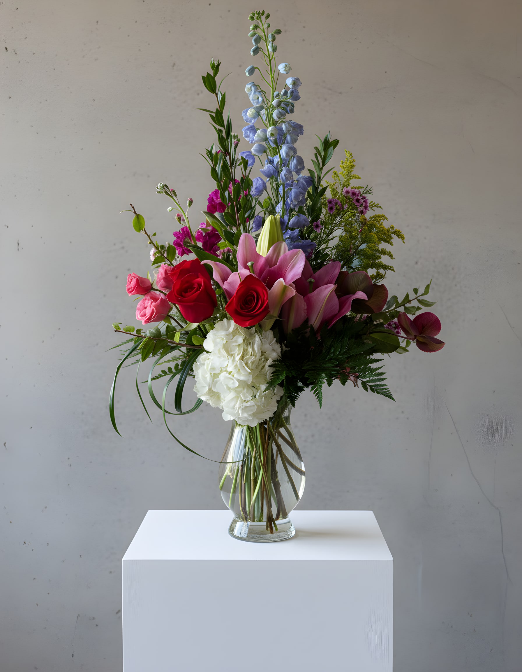 Mixed bouquet with roses, lilies, hydrangea, and blue delphinium in a glass vase