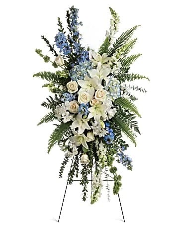 Standing floral spray with white lilies, cream roses, and blue flowers