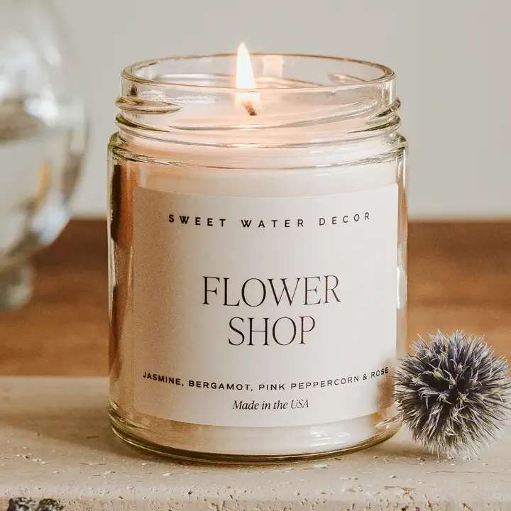 Lit candle in a clear glass jar labeled Flower Shop