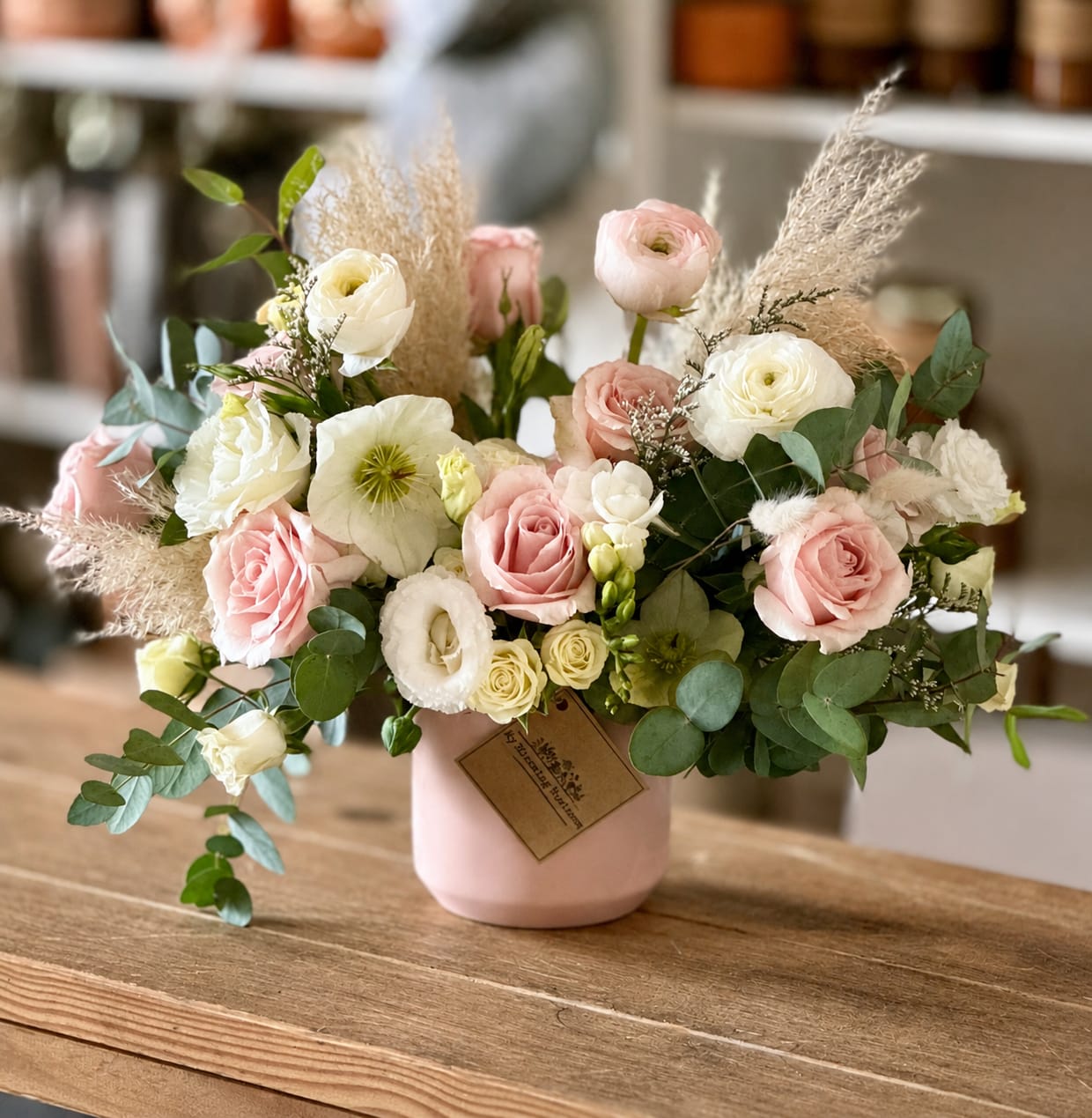 Pink and white roses in a blush vase with airy dried grasses
