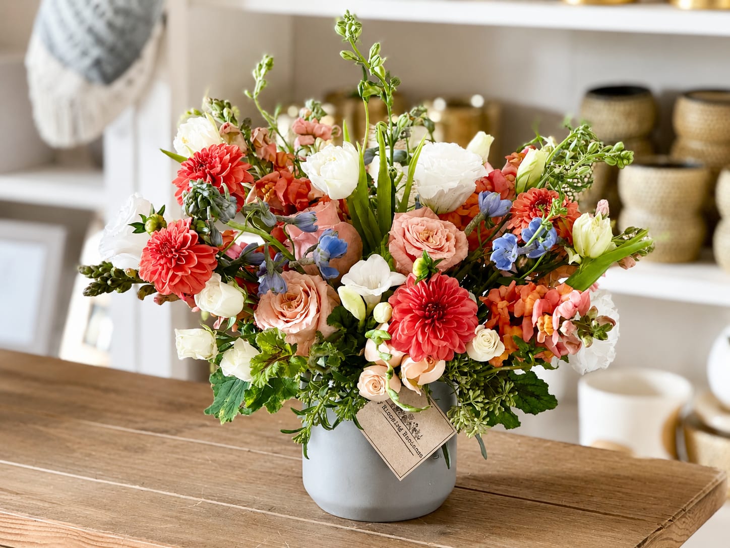 Mixed bouquet of coral, white, and blue flowers in a gray vase