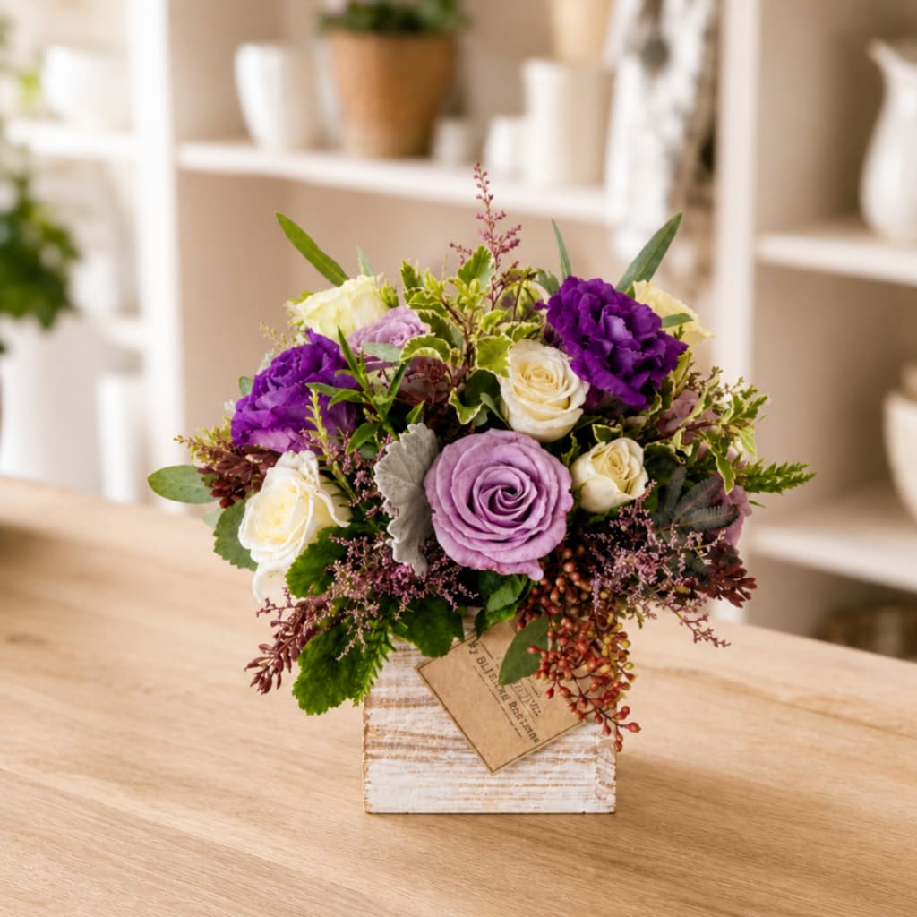 Purple and cream rose arrangement in a rustic white vase