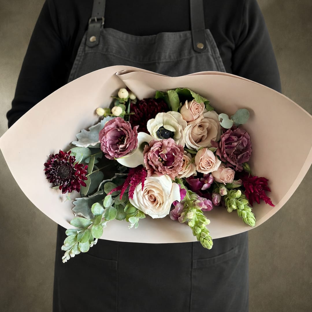 Handheld bouquet of blush roses, white anemones, and burgundy blooms in pale wrap