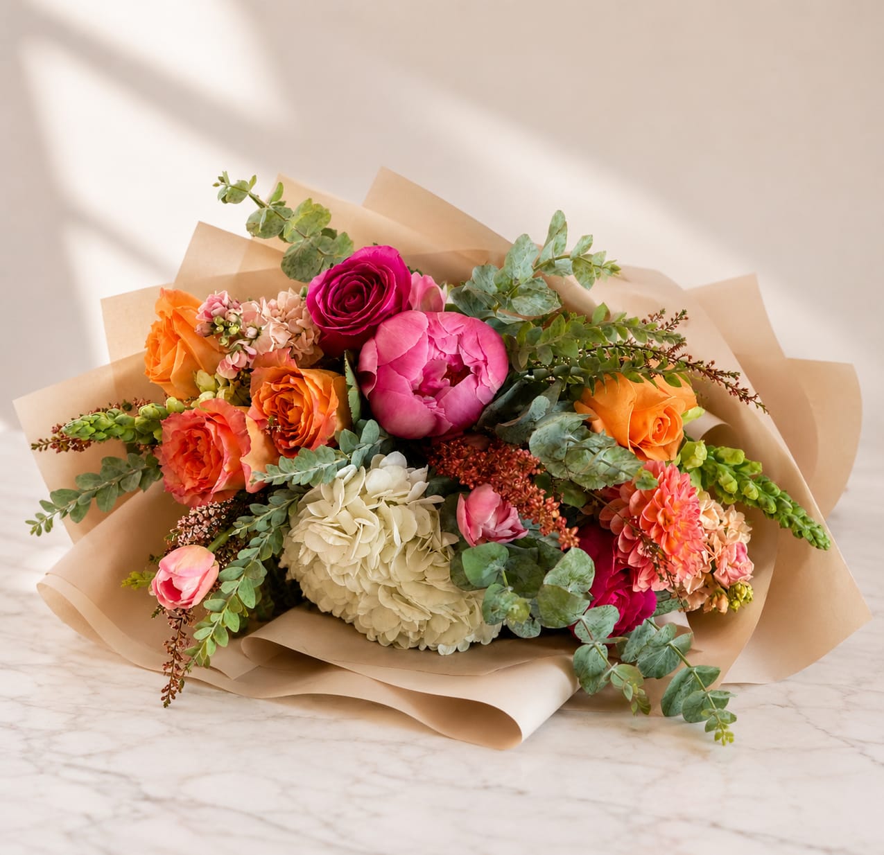 Mixed bouquet of roses, peonies, and hydrangea wrapped in kraft paper