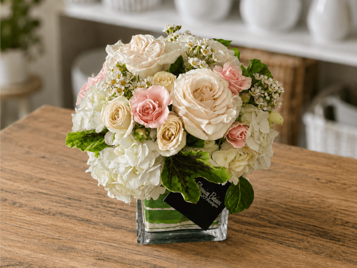 Compact bouquet of cream and pink roses in a clear square vase