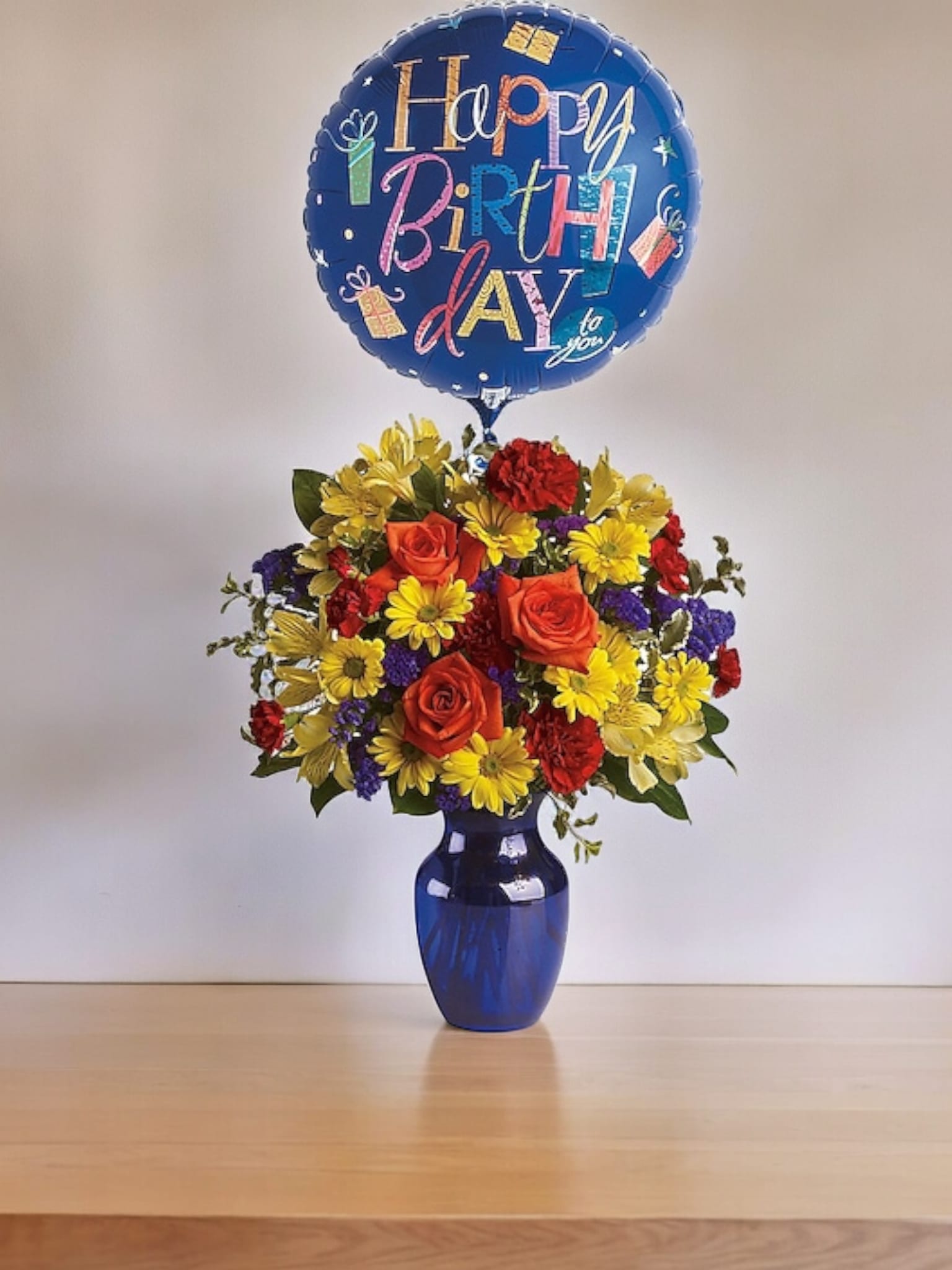 Birthday balloon above a colorful flower arrangement in a blue vase
