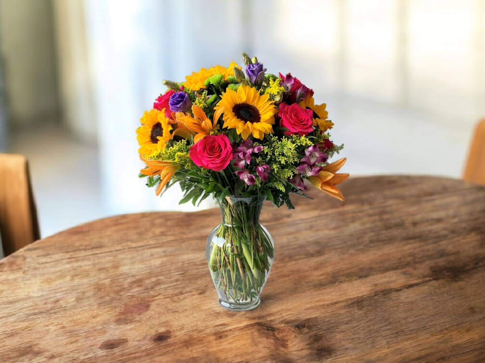 Mixed bouquet of sunflowers, roses, and lilies in a glass vase