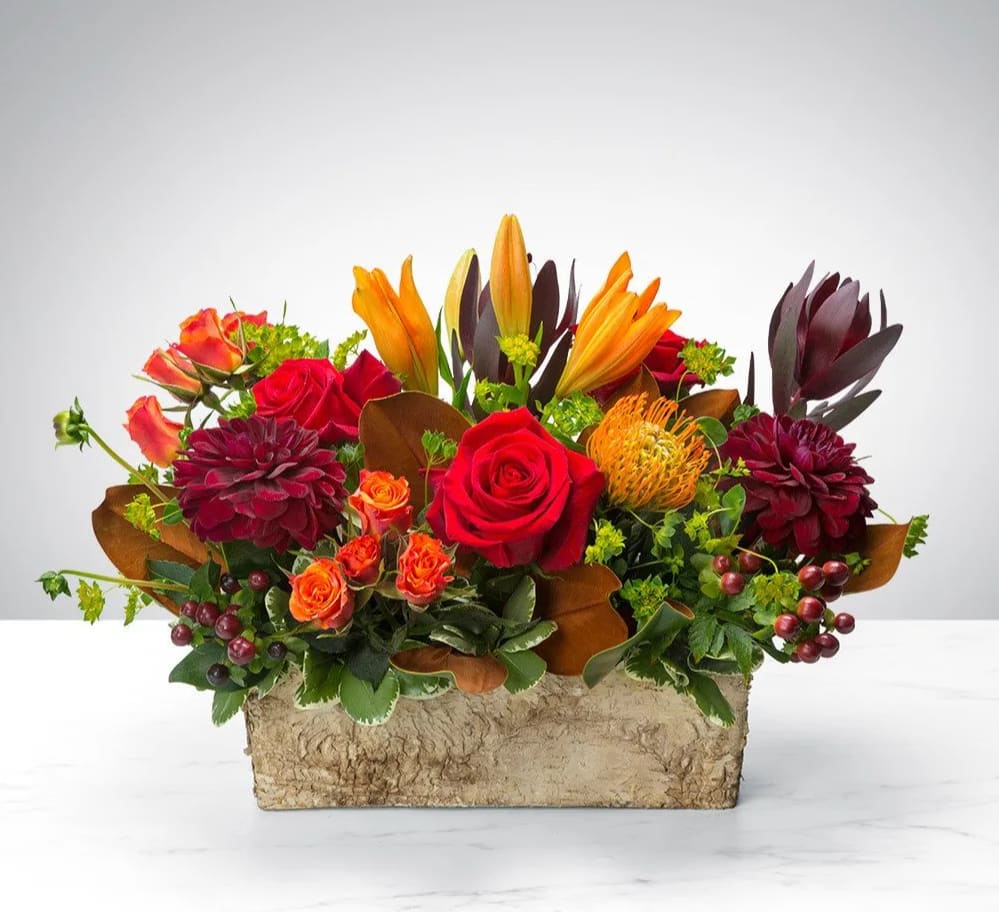 Mixed bouquet with red roses, orange lilies, and burgundy blooms in a rectangular container