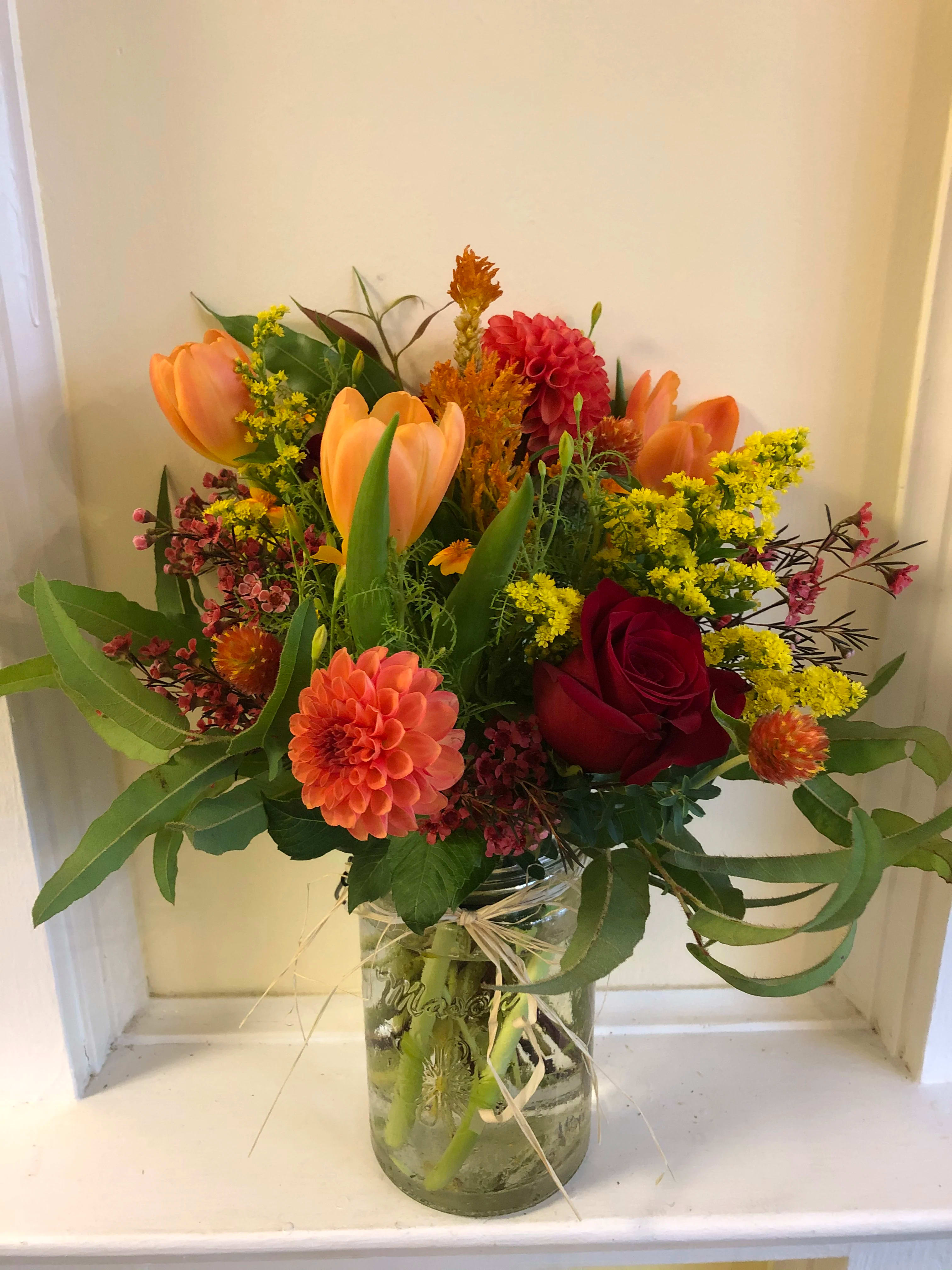 Mixed bouquet of orange tulips, red roses, and a peach dahlia in a glass jar