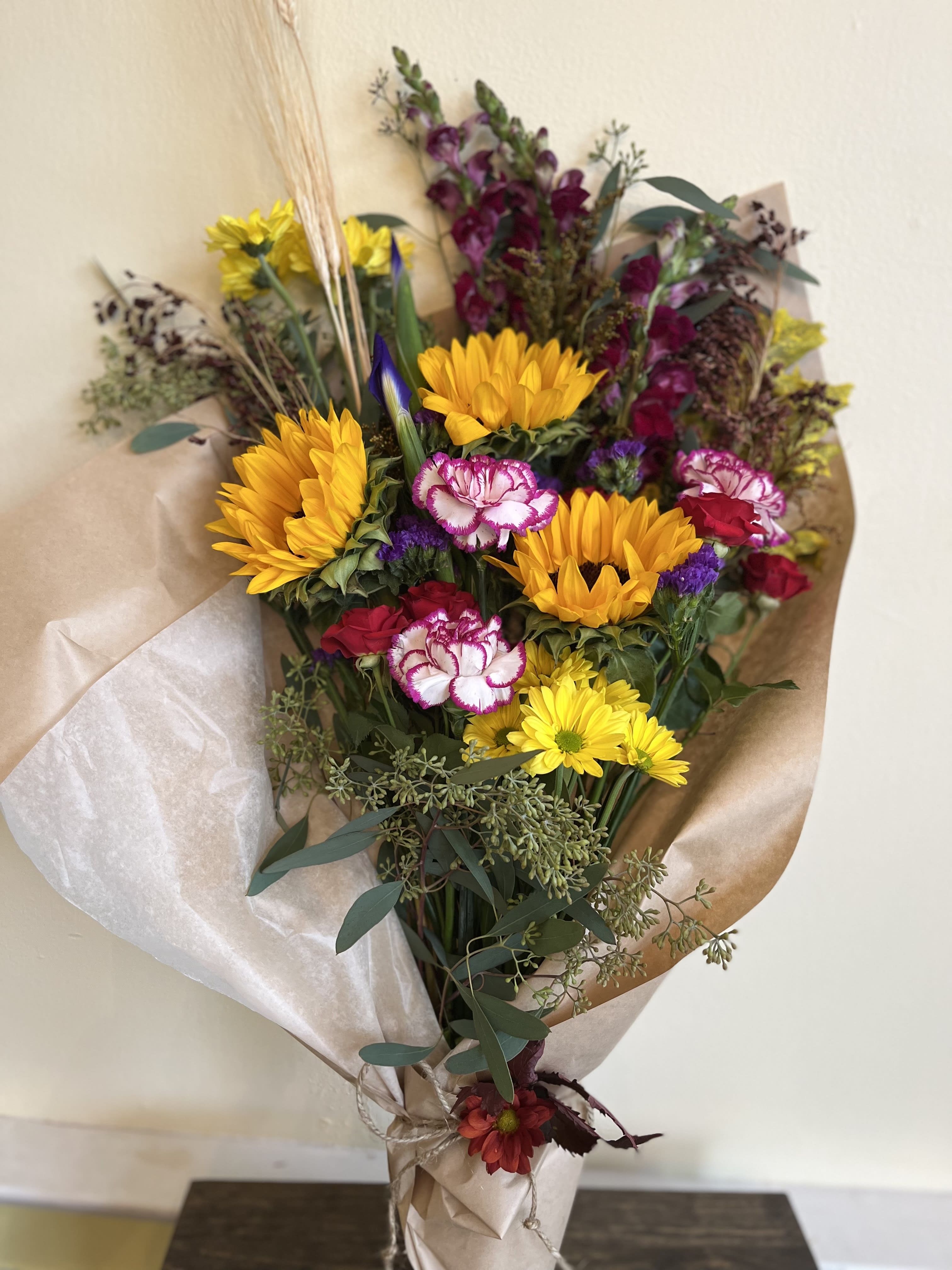 Bouquet of yellow sunflowers, pink carnations, and purple flowers wrapped in paper