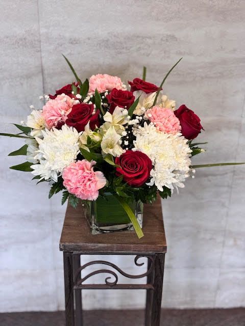 Bouquet of red roses, pink carnations, and white chrysanthemums in a glass vase