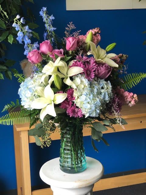 Bouquet of pink roses, lilies, hydrangeas, and blue delphinium in a glass vase