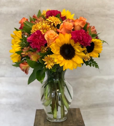 Mixed bouquet with sunflowers, roses, and mums in a clear glass vase
