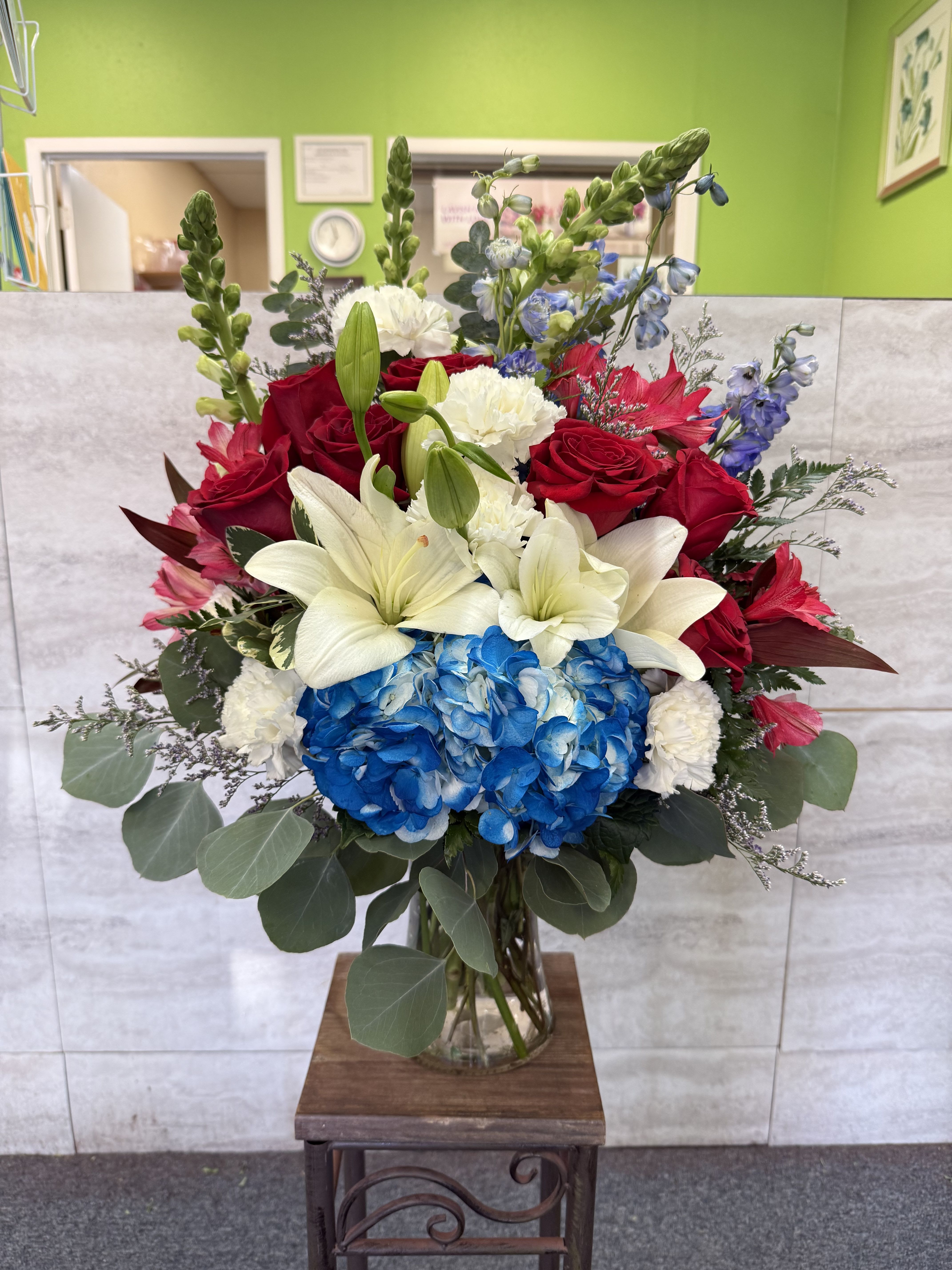 Bouquet of red roses, white lilies, and blue hydrangeas in a glass vase