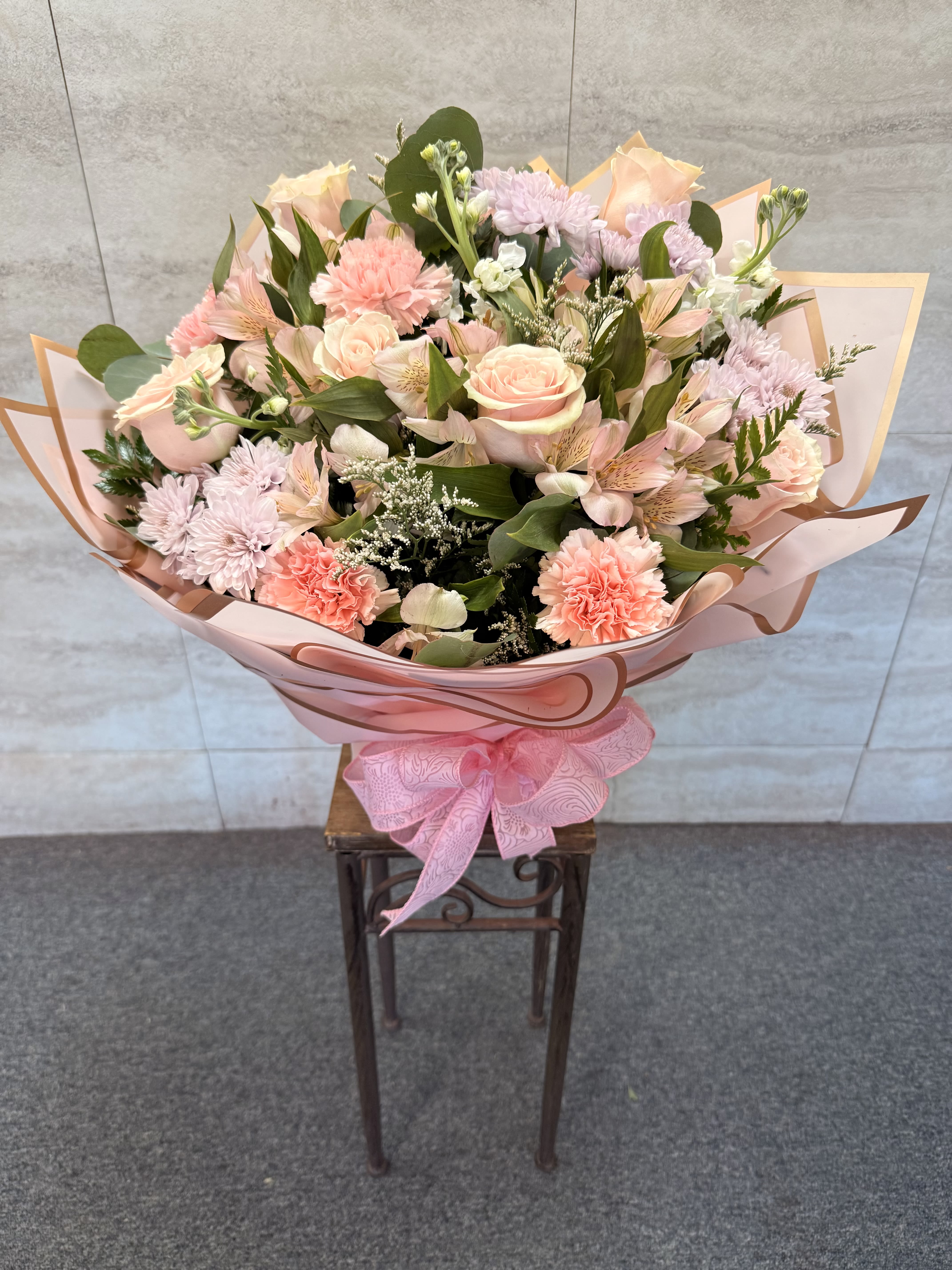 Large bouquet of pink and peach flowers wrapped in pink paper with a ribbon