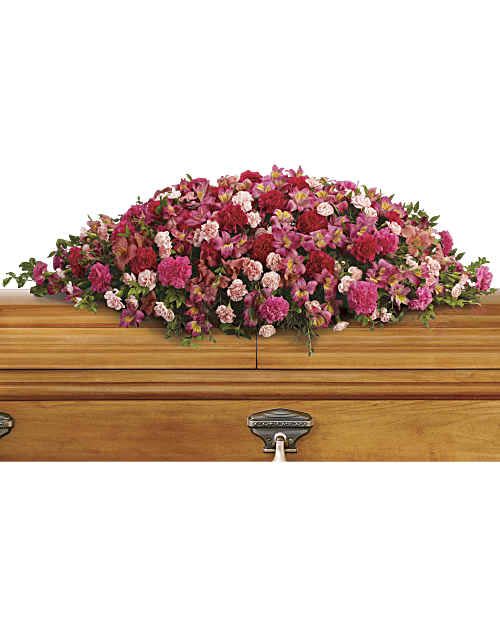Pink and red floral casket spray on a wooden casket