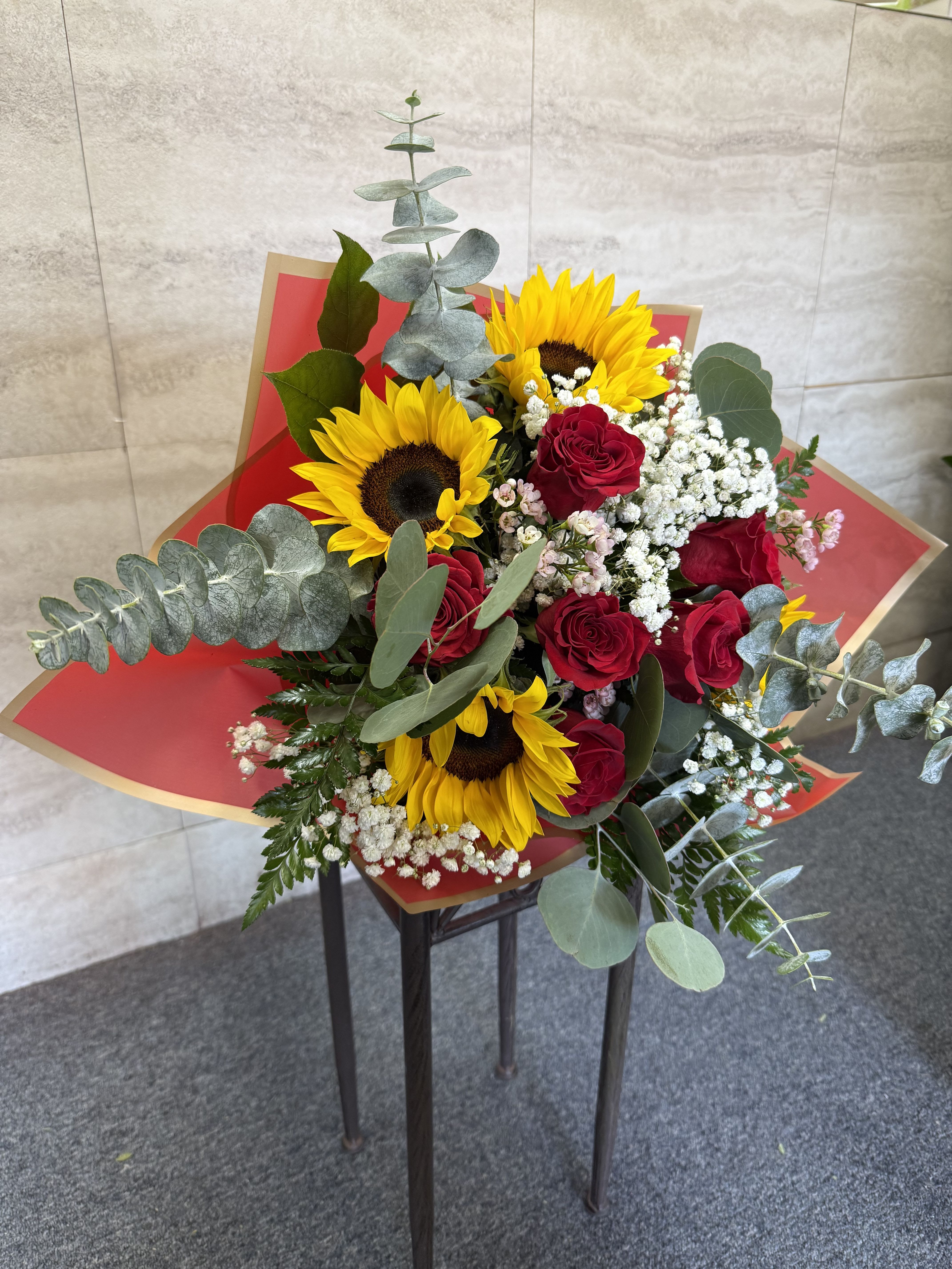 Bouquet of red roses and yellow sunflowers with white filler in red wrap
