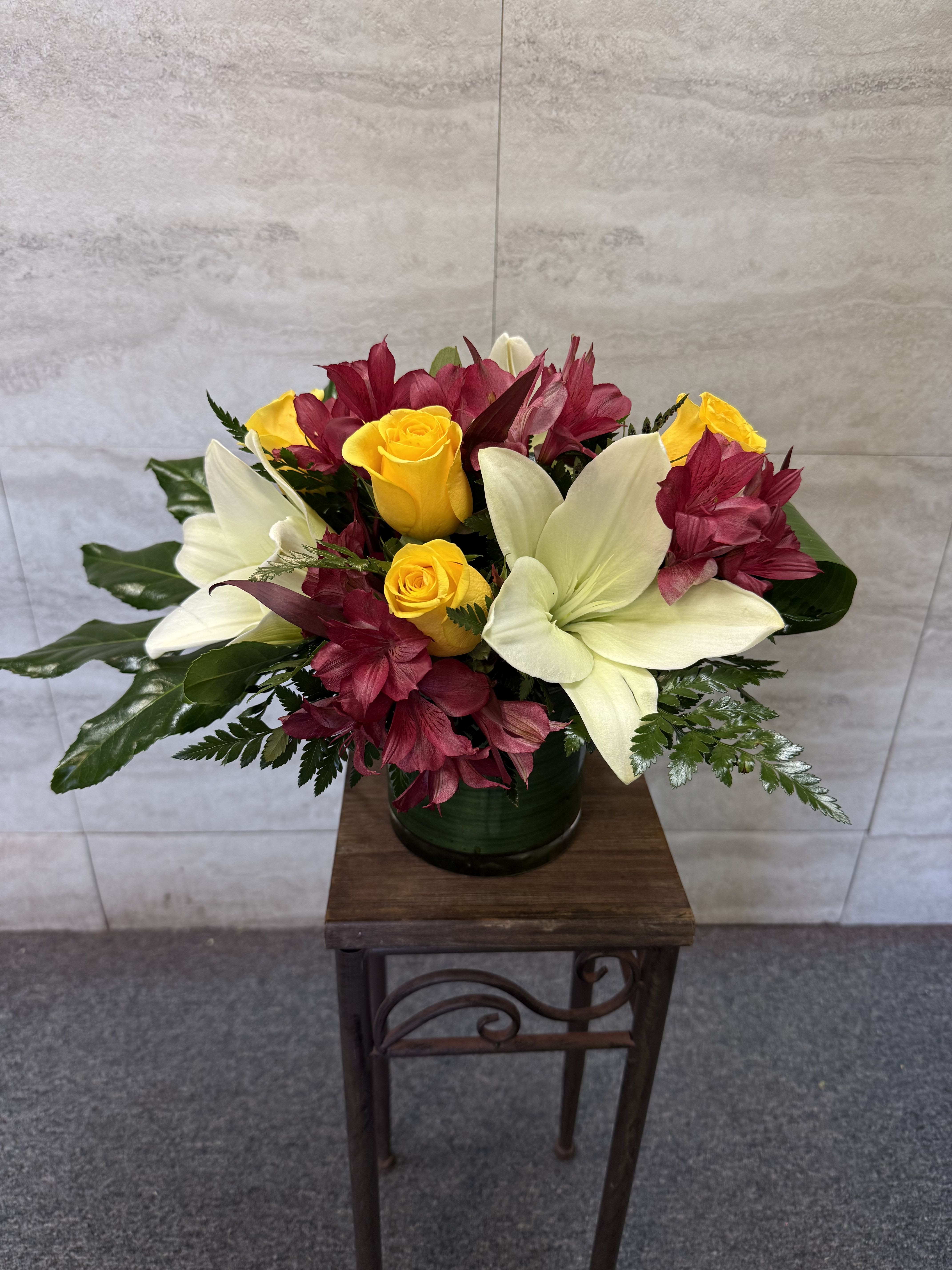 Bouquet of yellow roses and white lilies with burgundy flowers in a dark vase