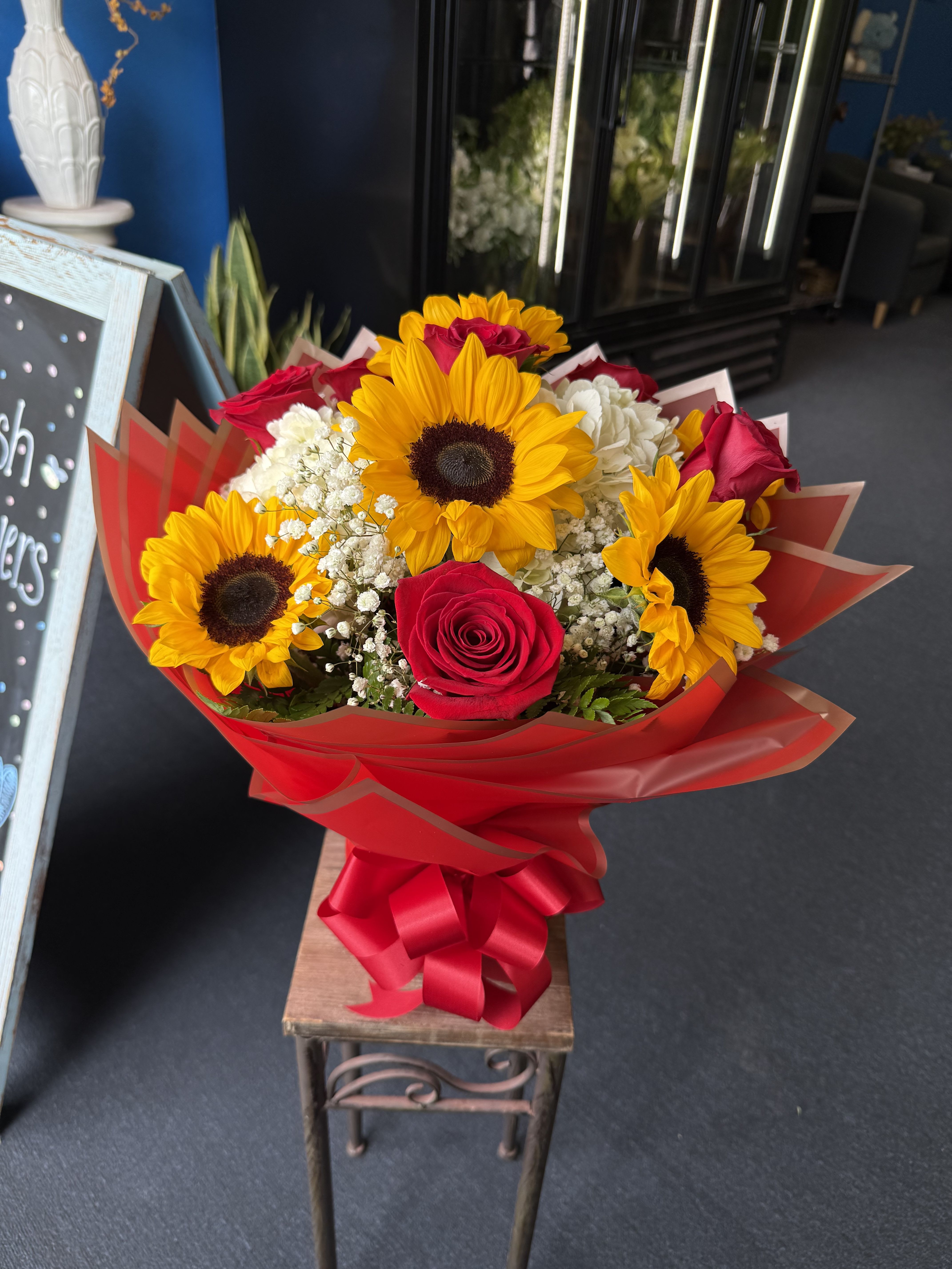 Love and Sunshine  - Bright sunflowers, vivid red roses and white accents wrapped in bold red paper with a satin ribbon-cheerful, romantic bouquet perfect for celebrations, birthdays, or heartfelt congratulations.