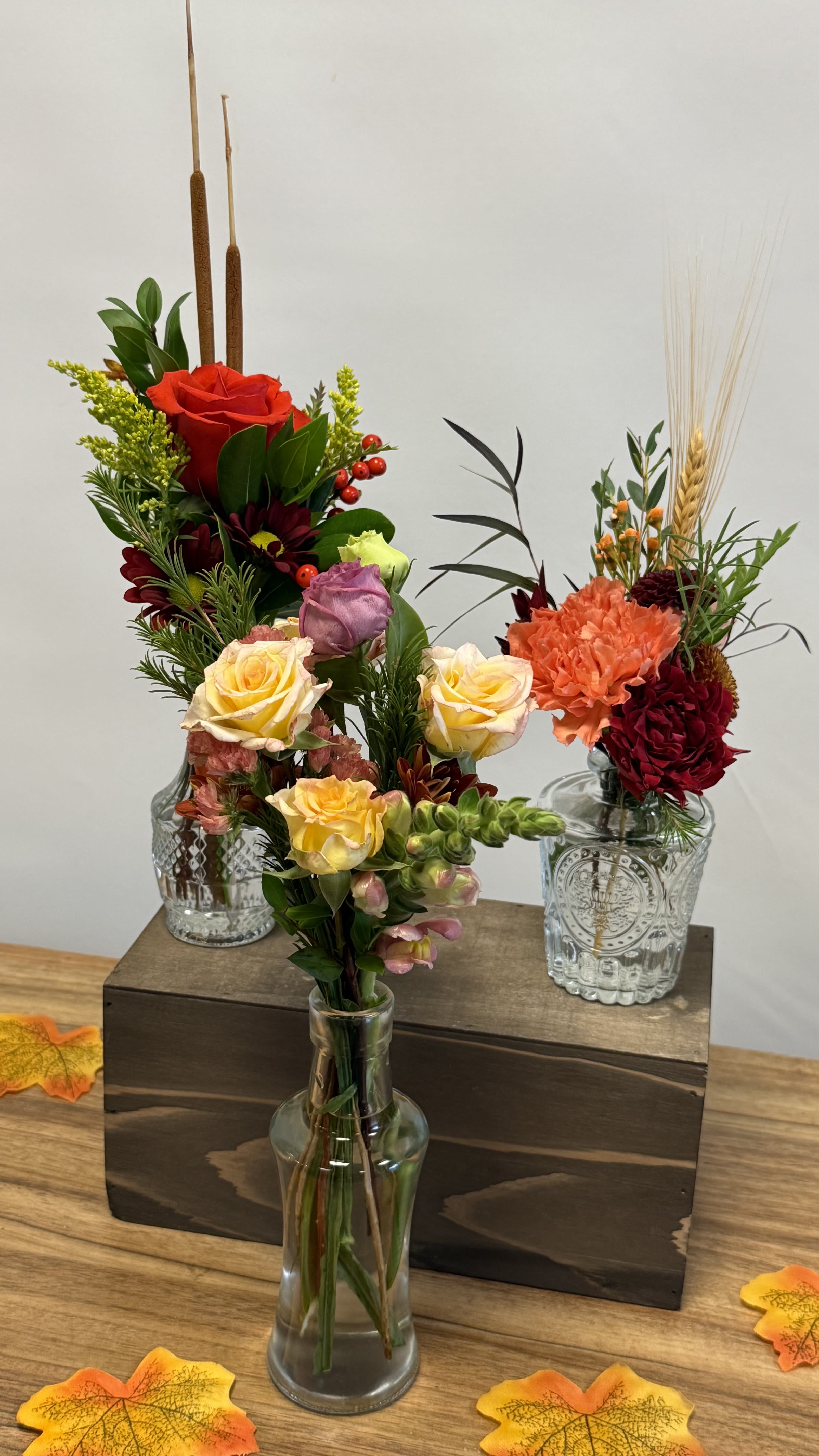 Three floral arrangements in glass vases with roses and carnations