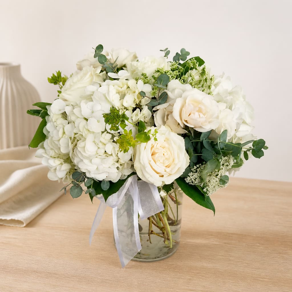 White roses and hydrangeas arranged in a glass vase with a ribbon