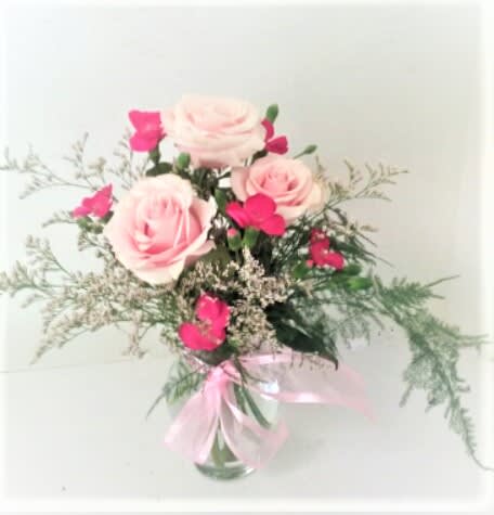 Pink roses and hot pink blooms in a clear vase with a pink ribbon