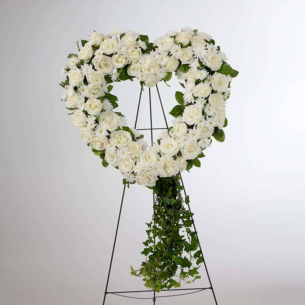 White rose heart wreath on a black easel with trailing greenery