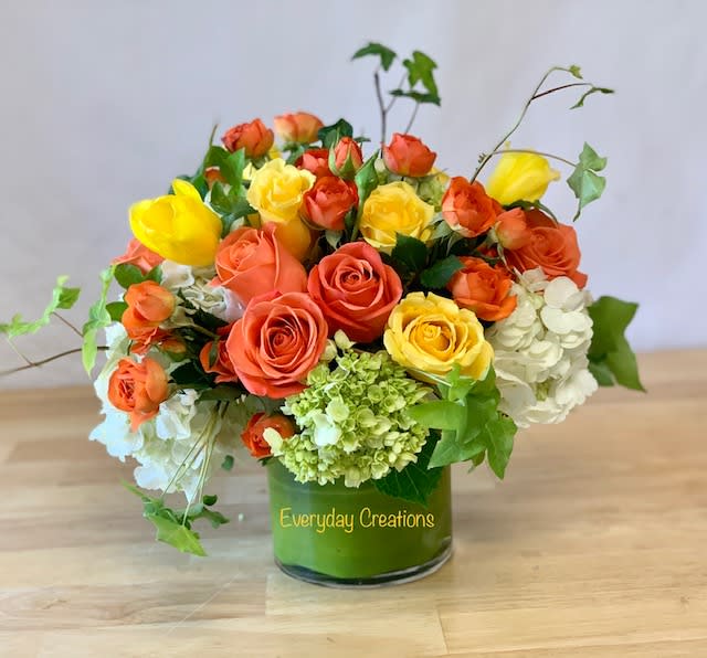 Orange and yellow roses with white hydrangeas in a glass vase
