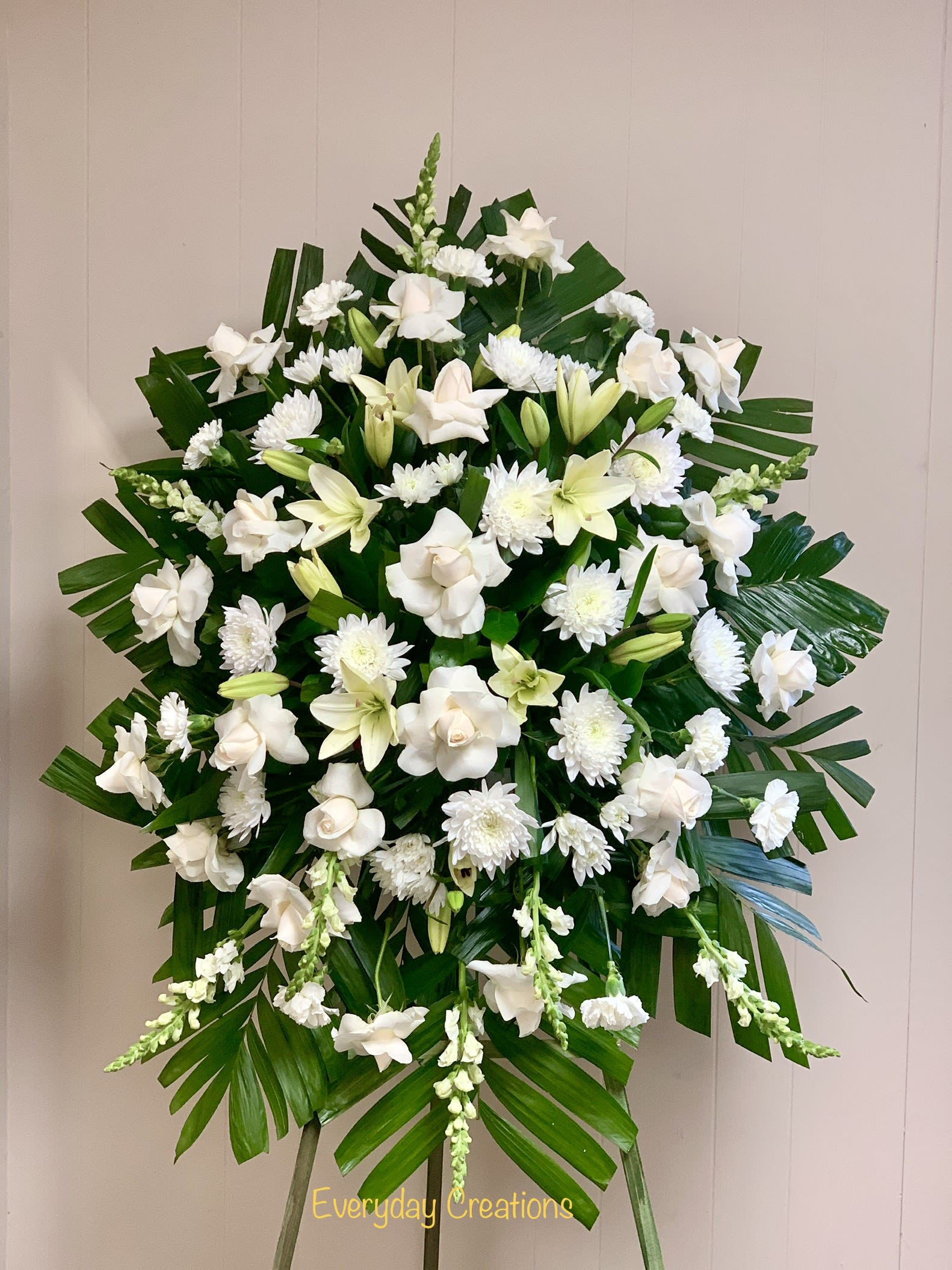 Large standing spray of white roses, lilies, and mums with bold green foliage
